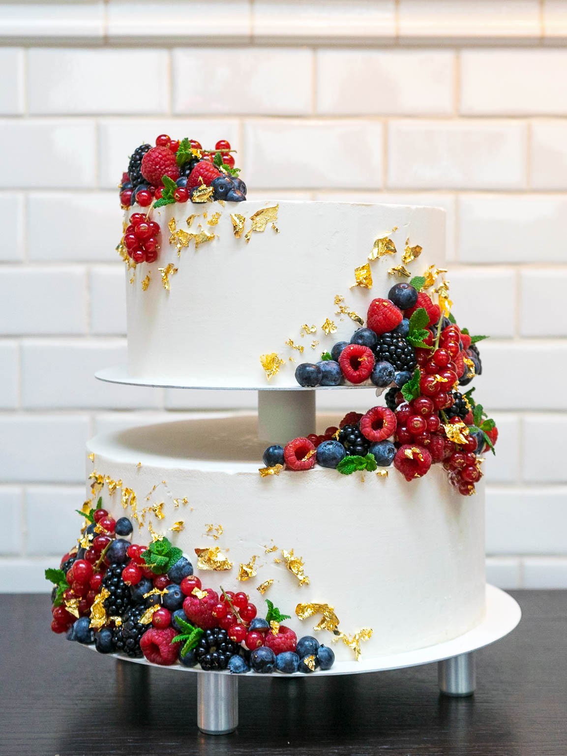 Zweistöckige weiße Hochzeitstorte mit frischen Beeren und Blattgold
