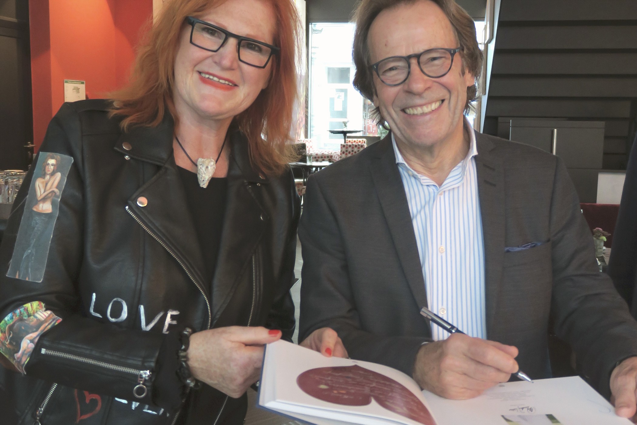 Mann signiert ein Buch neben einer lächelnden Besucherin bei einem Event im Andreas Quartier