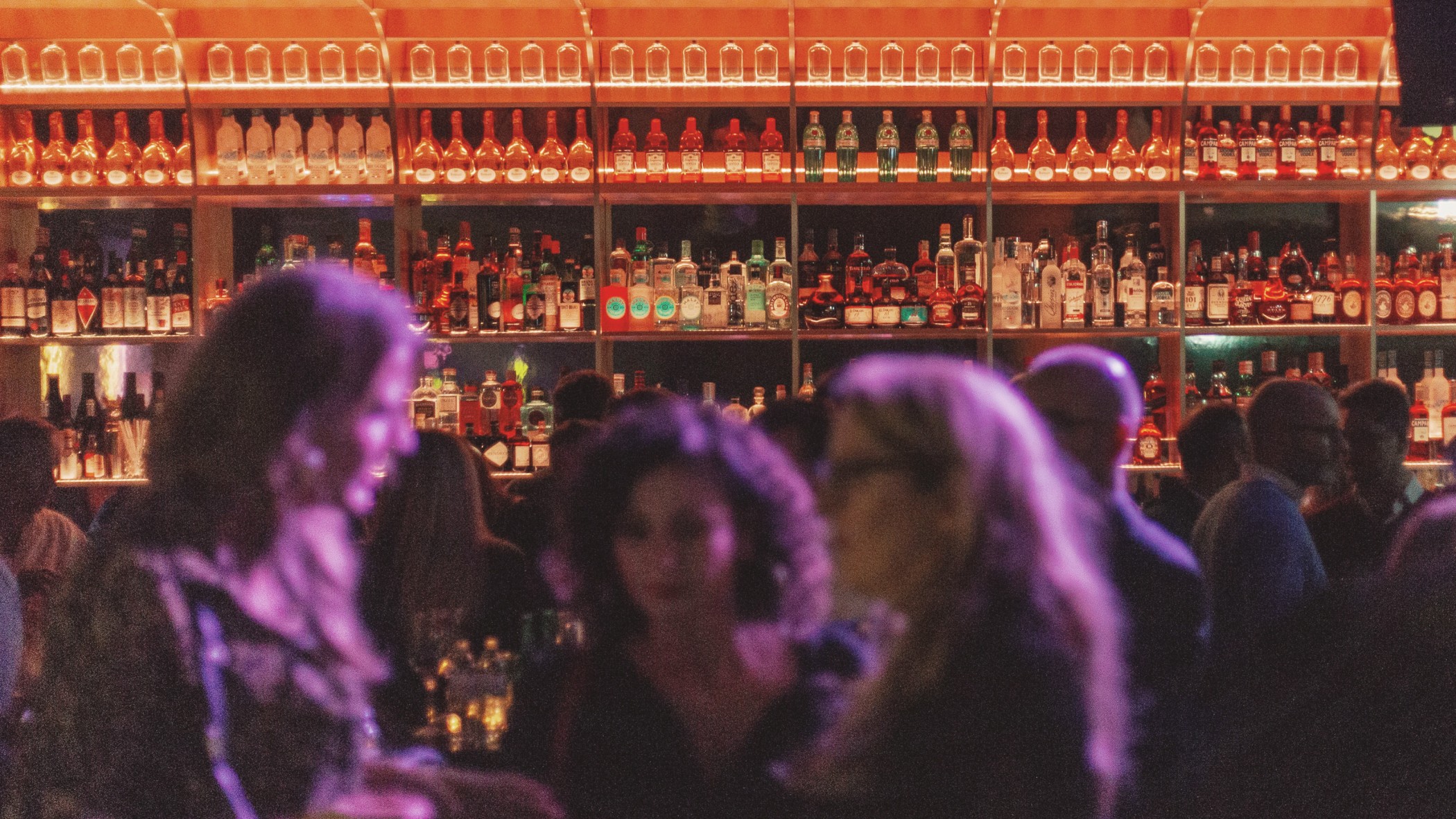 Gäste im violetten Licht vor der Flaschenwand der Bar
