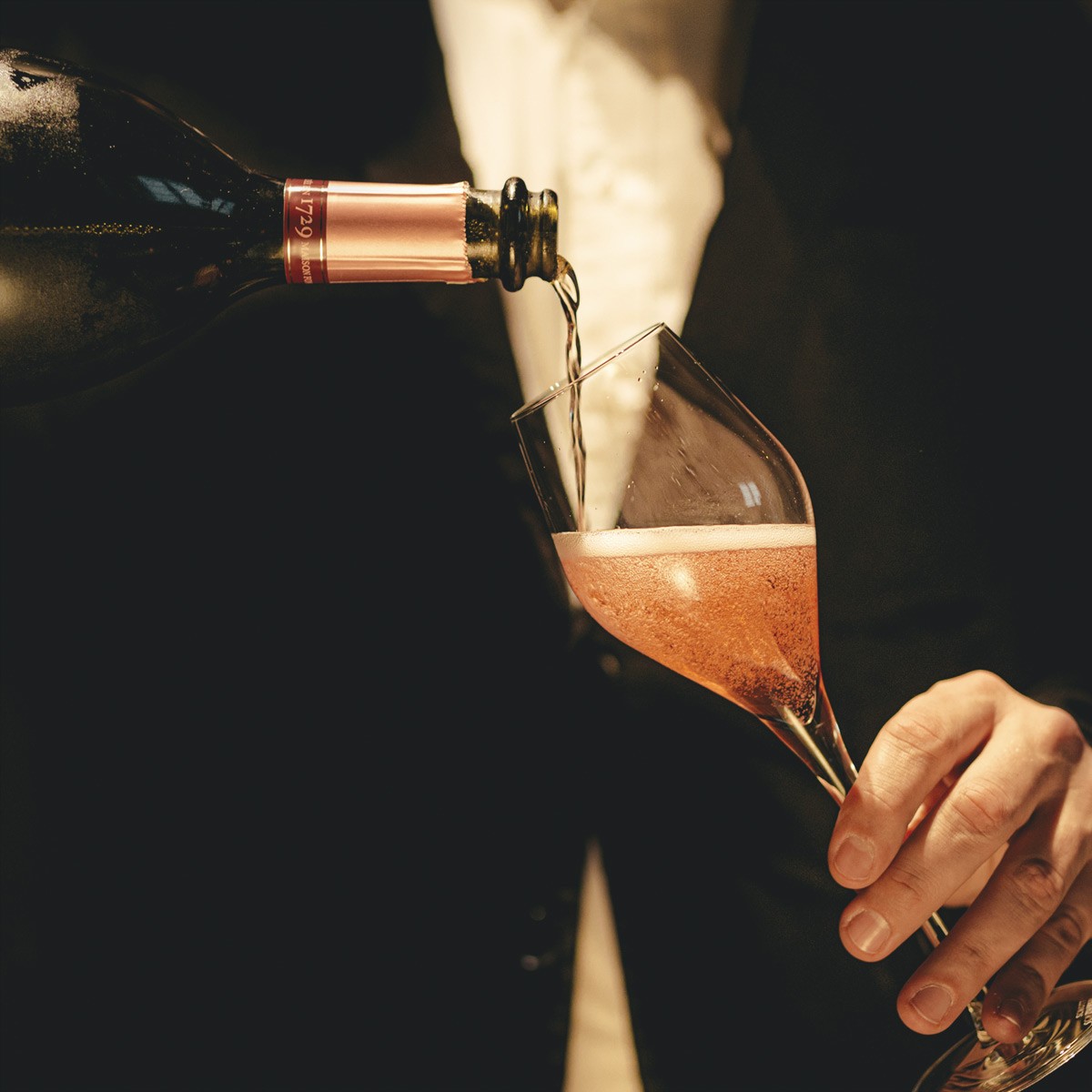 Nahaufnahme: Roséchampagner fließt aus der Flasche in ein Glas