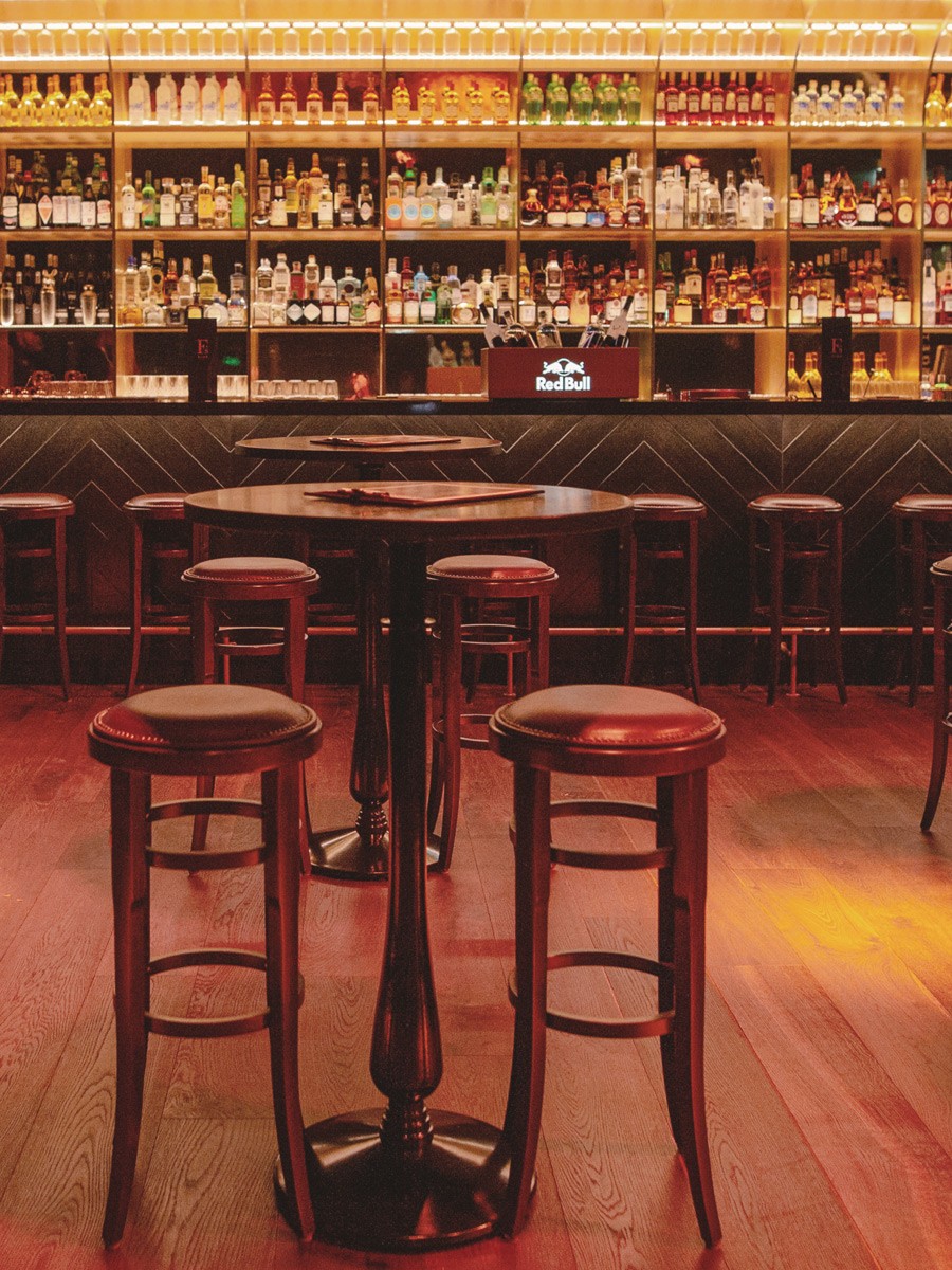 Stehtisch mit Barhockern aus Holz vor der beleuchteten Bar