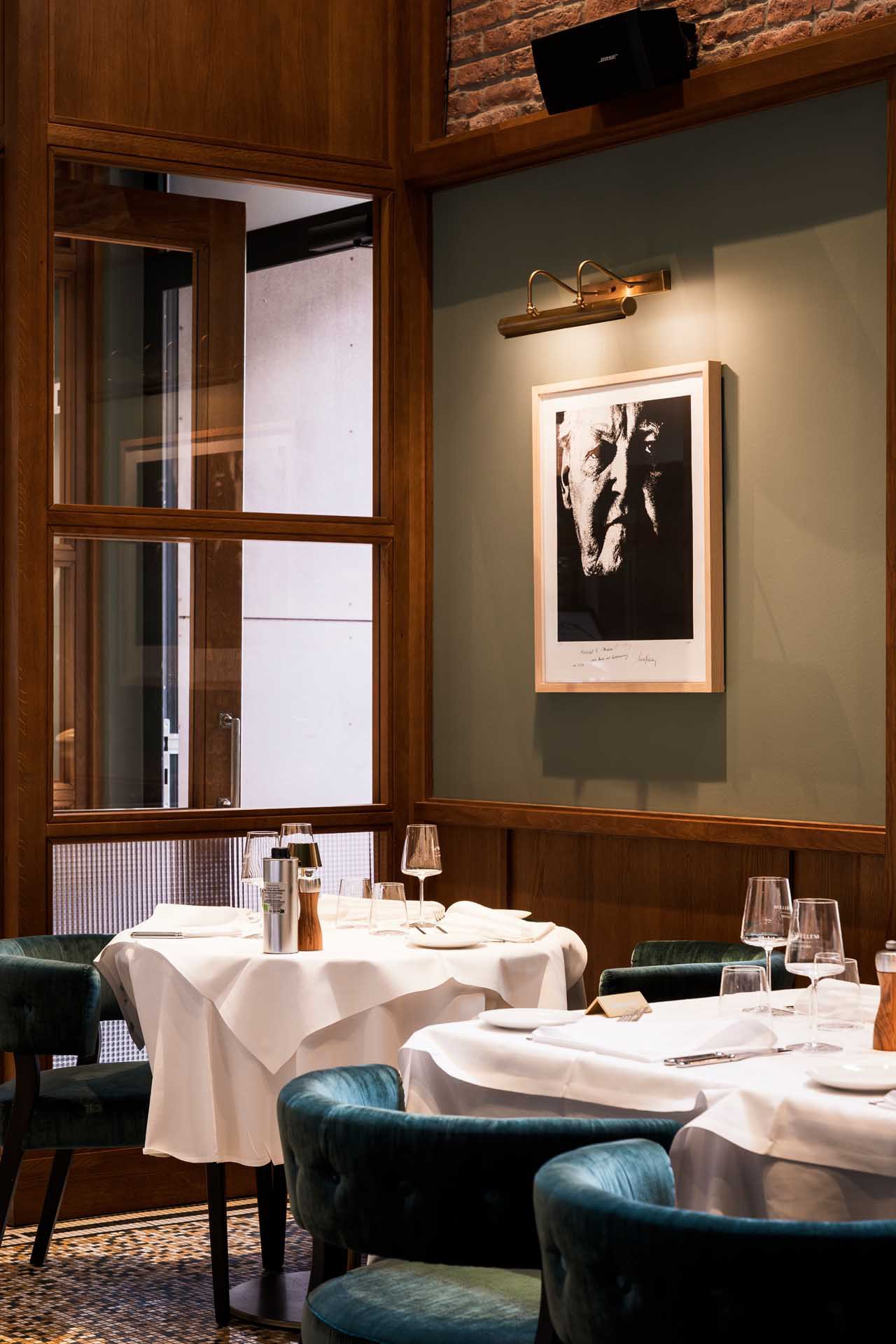 Laid tables with green armchairs at il punto beneath a black-and-white portrait