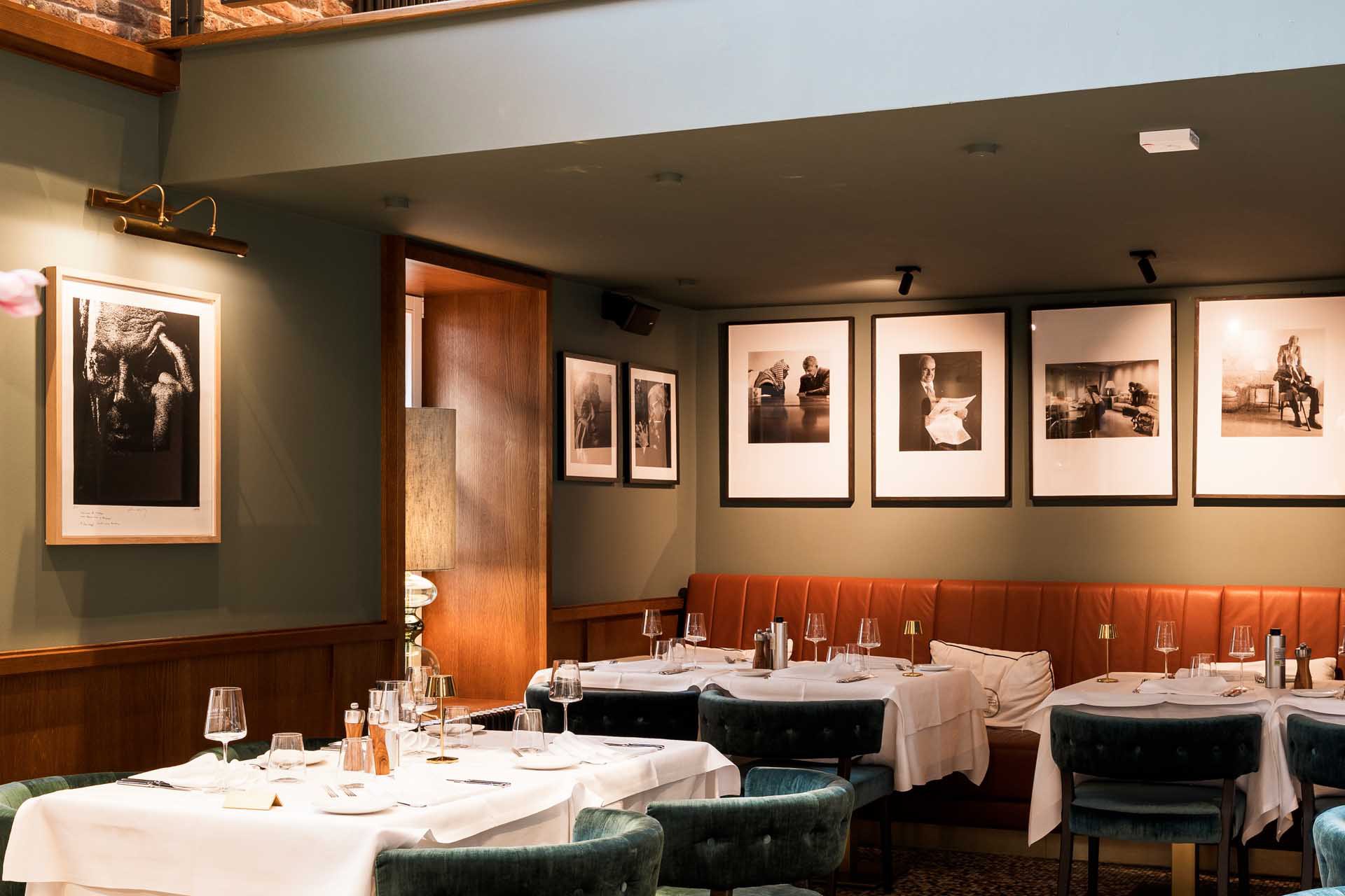 White-clothed tables at il punto in front of black-and-white photographs on a green wall