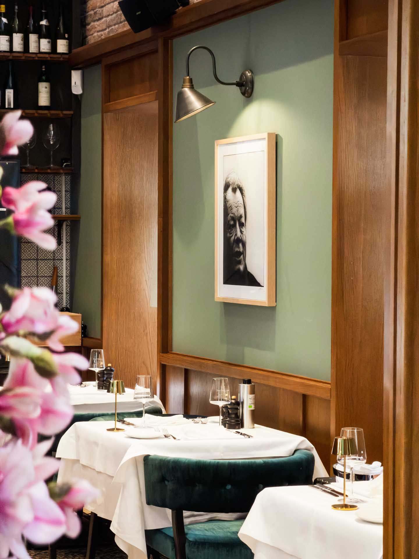 Restaurant il punto mit weiß gedeckten Tischen, grüner Wand, Schwarz-Weiß-Porträt und Kirschblüten