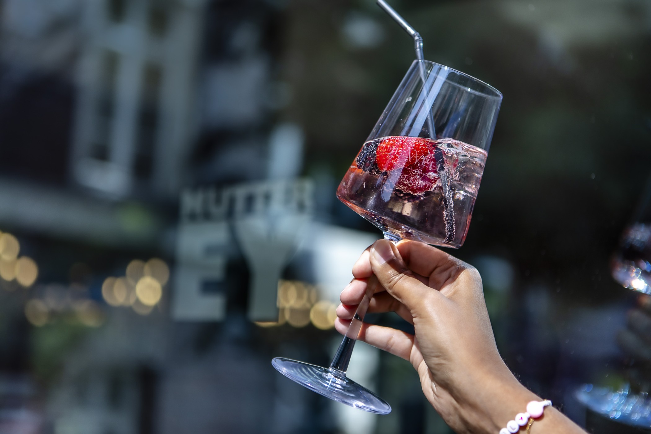 Hand hält ein Weinglas mit Beeren-Spritz vor dem Schriftzug des Mutter Ey Café
