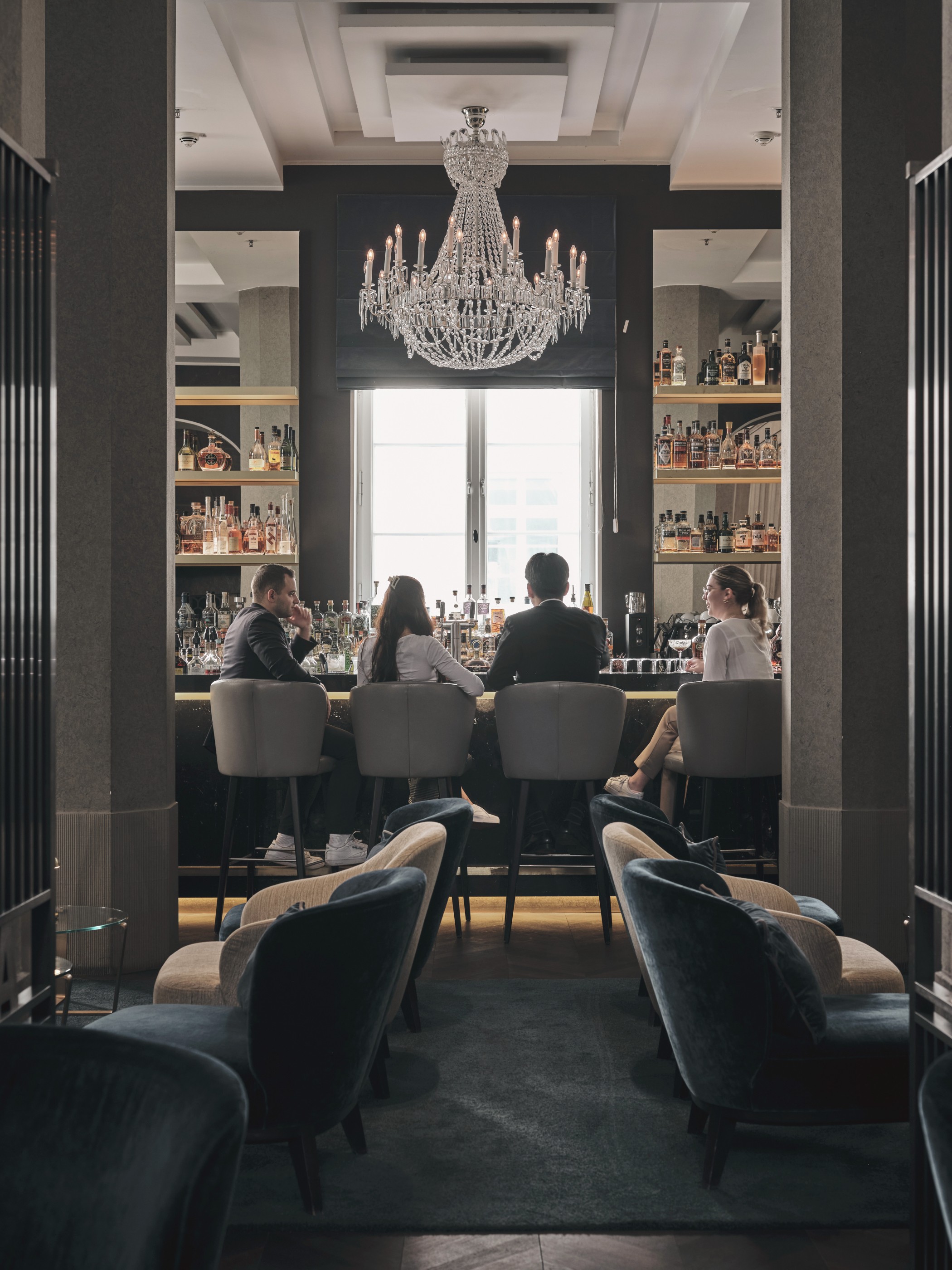 Gäste an der Theke der THE WELLEM Bar unter einem Kristallleuchter, davor Lounge-Sessel