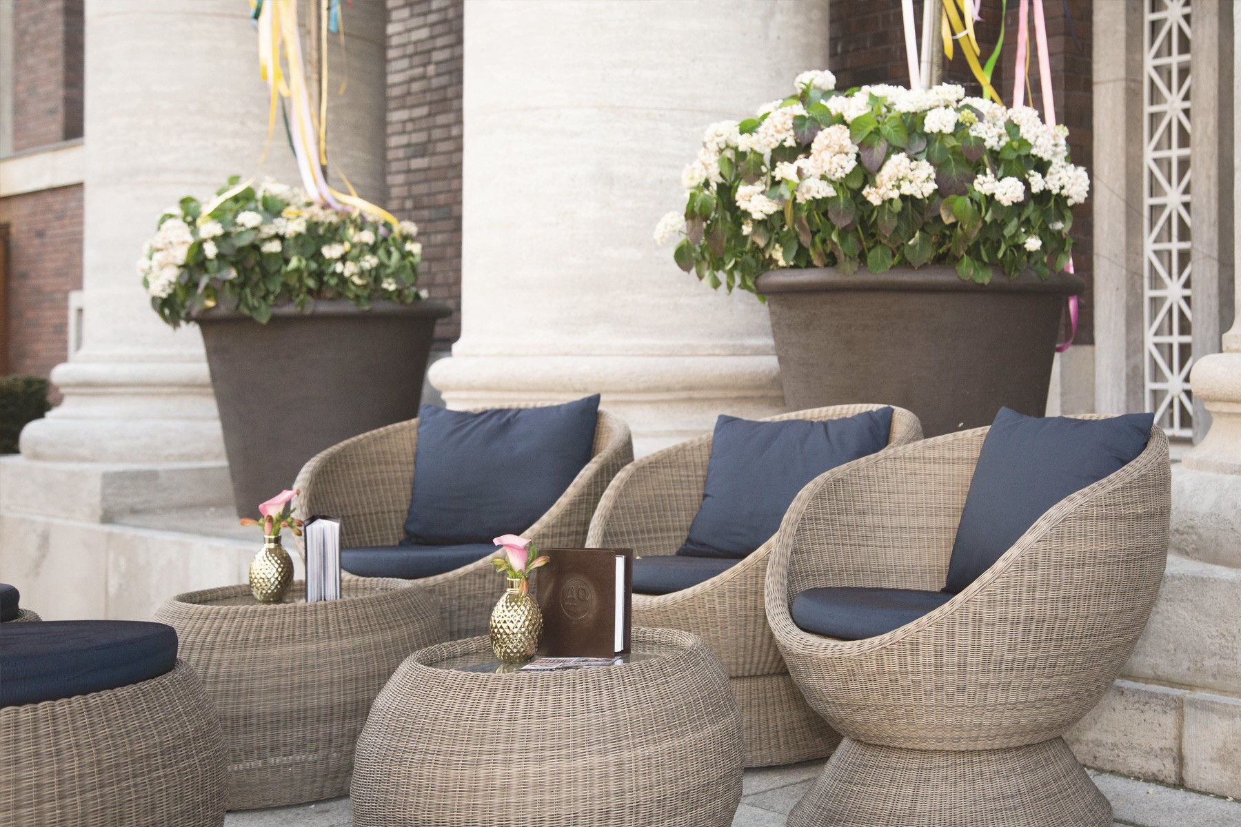 Terrasse von The Wellem mit Korbsesseln, blauen Kissen und Blumenkübeln zwischen Säulen