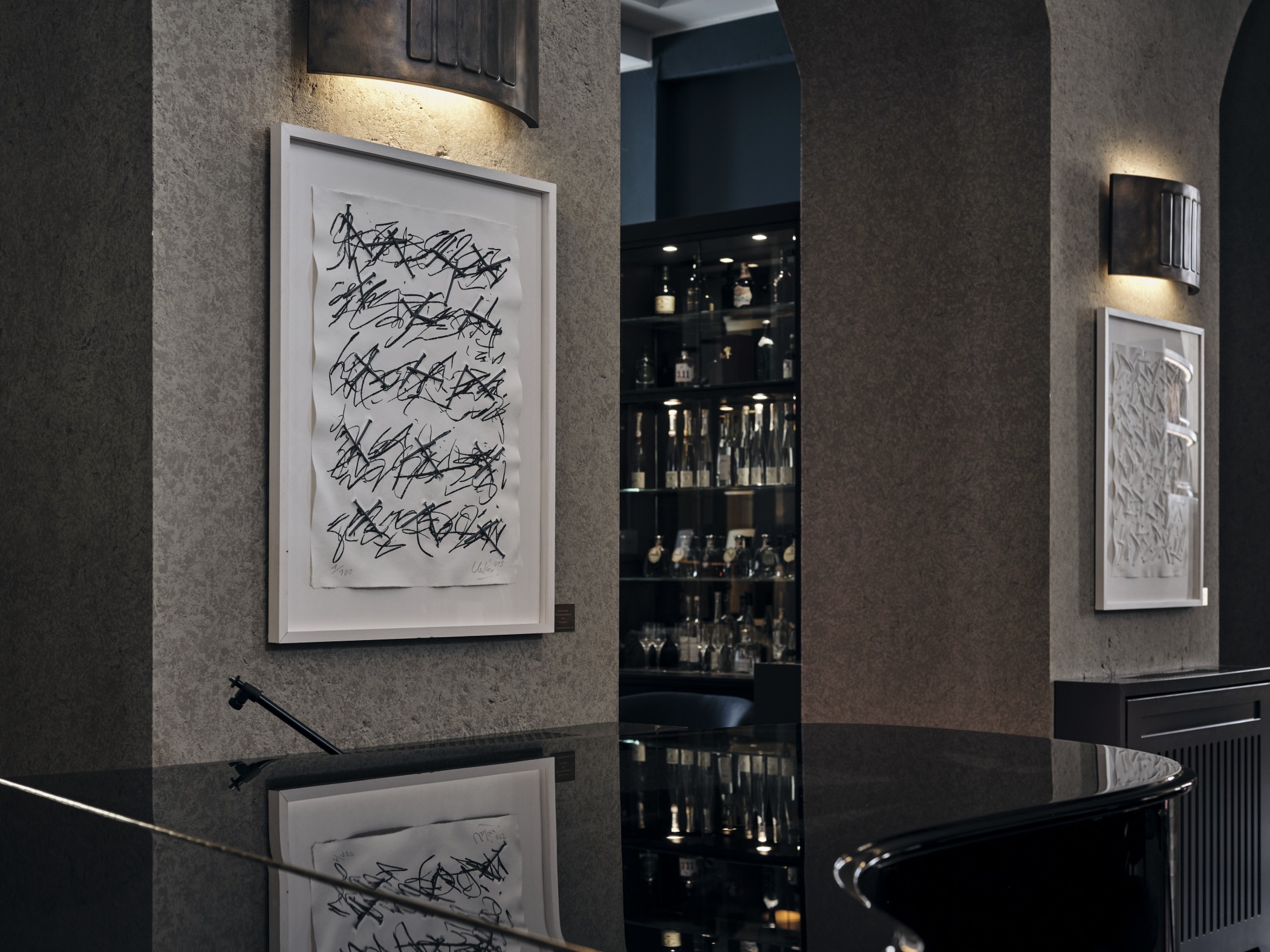Kunstwerke von Günther Uecker an den Wänden der THE WELLEM Bar neben beleuchteten Flaschenregalen