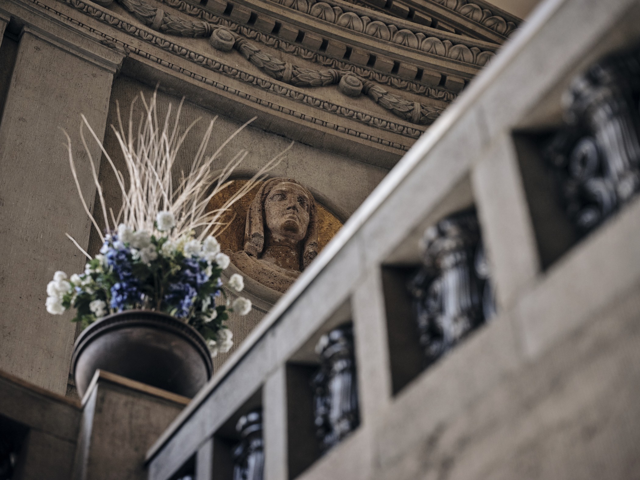 Blumenschmuck auf der Steinbalustrade der historischen Halle von The Wellem mit Reliefkopf im Hintergrund