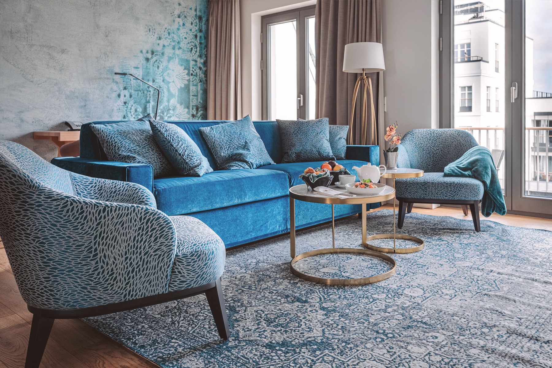 Wohnzimmer einer Residence mit blauem Sofa, gemusterten Sesseln und runden Couchtischen