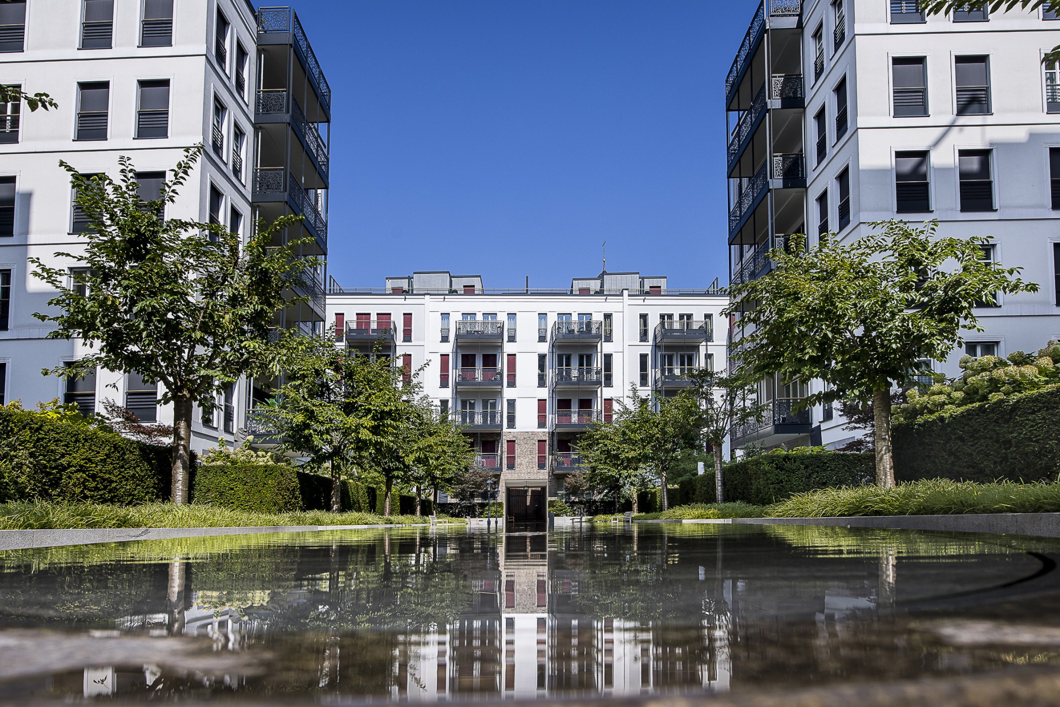 Innenhof des Andreas Quartiers mit Wasserbecken, in dem sich Bäume und Wohngebäude spiegeln