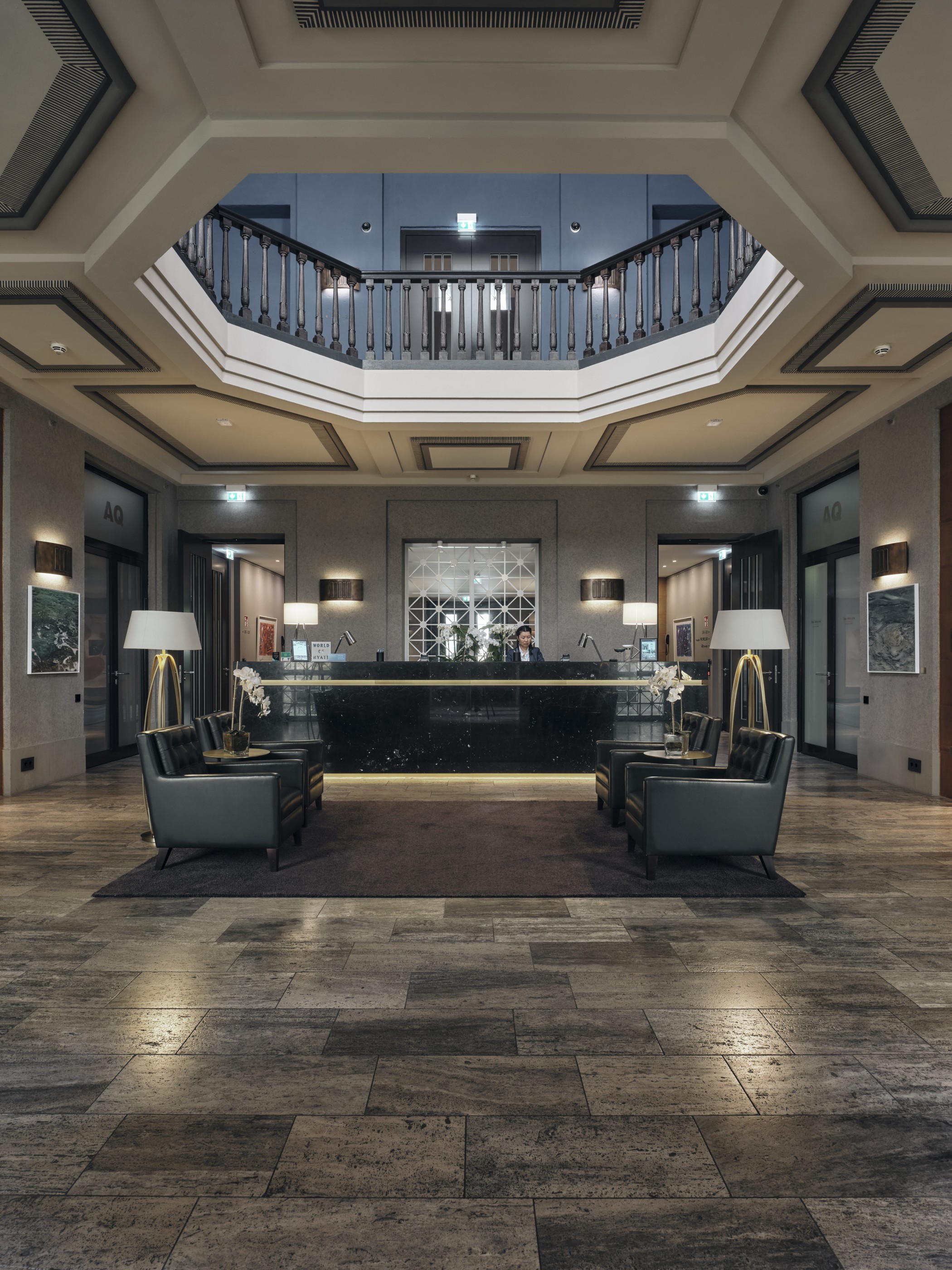 Rezeption und Lounge-Bereich von The Wellem mit Sesseln, Steinboden und umlaufender Galerie