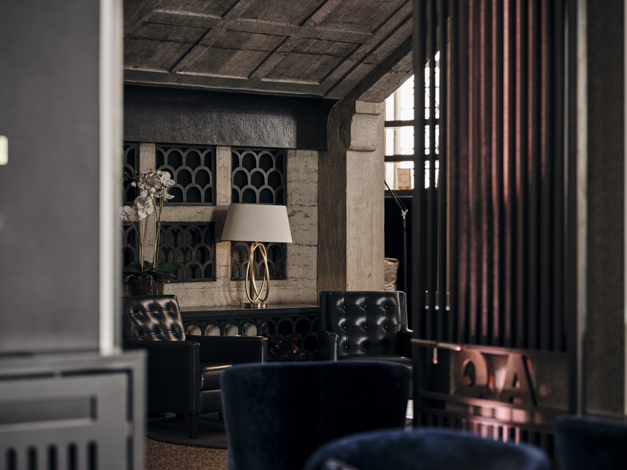 Lounge-Bereich in The Wellem mit dunklen Ledersesseln, Tischlampe und Weinregal in einer Wandnische