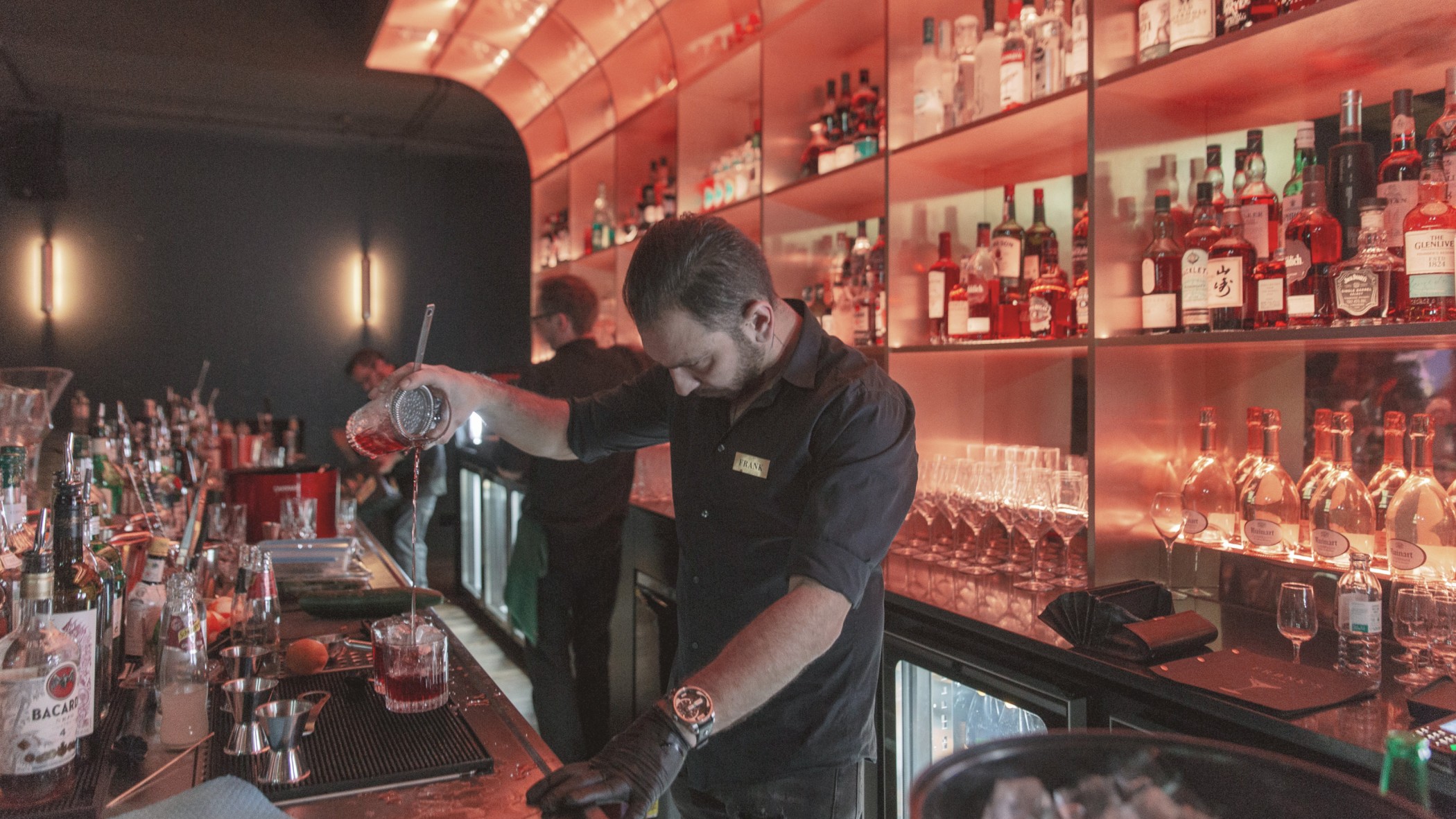 Barkeeper mixt einen Drink vor rot beleuchteten Flaschenregalen im FRANK'S Club