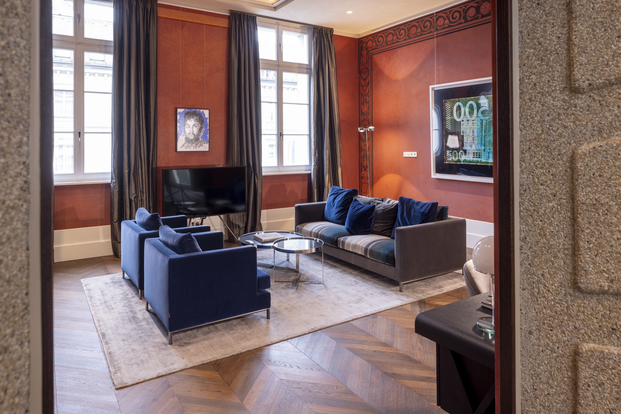 Wohnzimmer mit roten Wänden, blauen Samtsesseln, Sofa und Fernseher