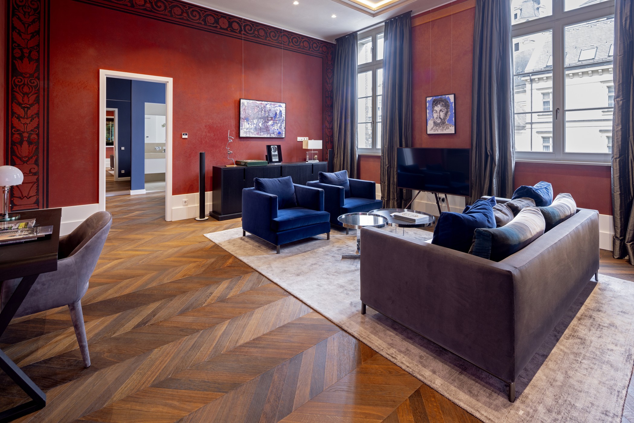 Großer Salon mit roten Wänden, Fischgrätparkett, blauen Sesseln und Sofa