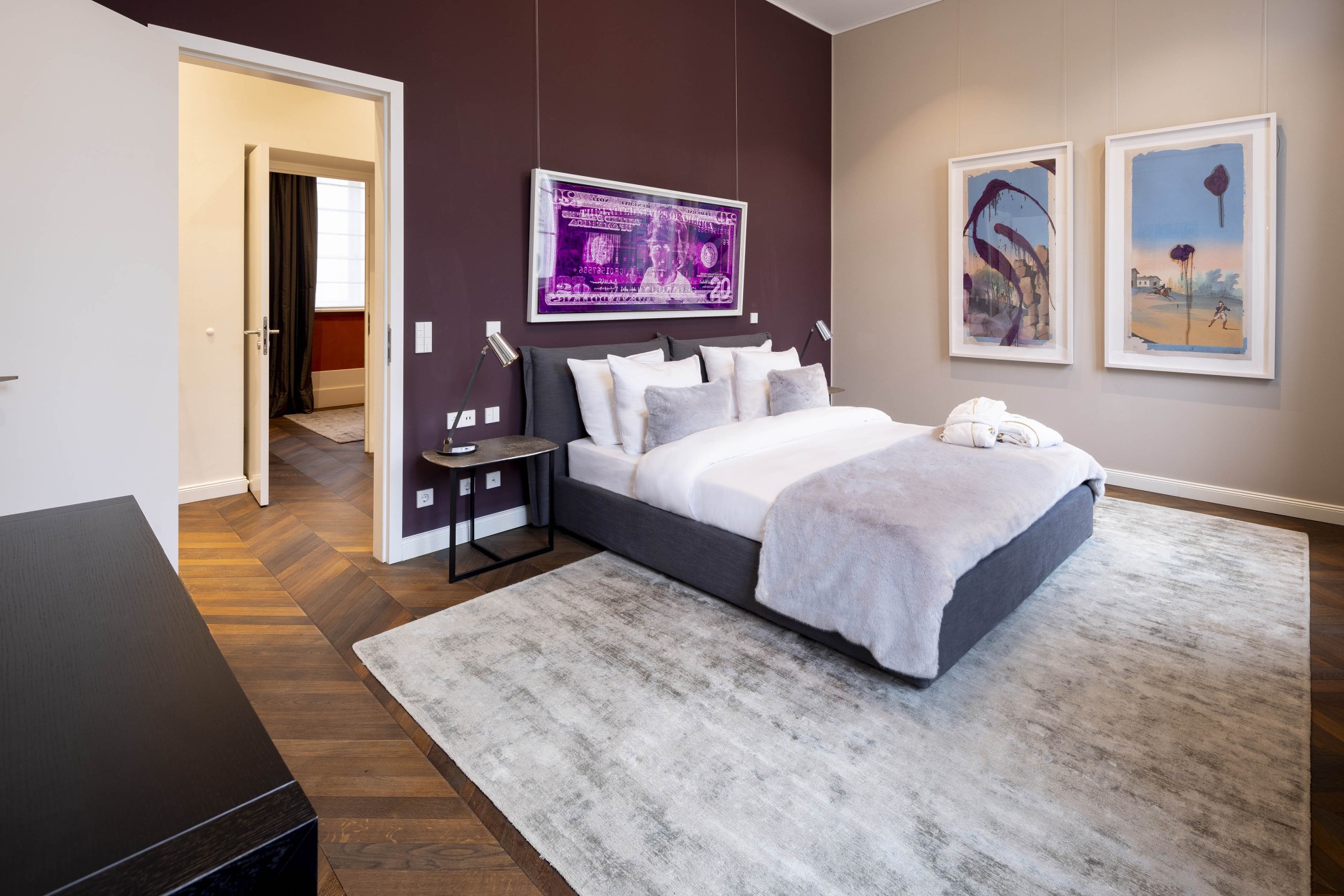 Schlafzimmer mit Doppelbett, auberginefarbener Wand und gerahmten Kunstwerken