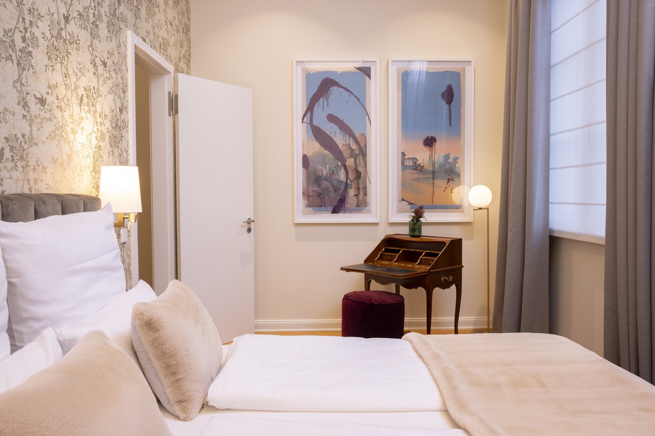 Schlafzimmer mit floraler Tapete, Sekretär und zwei gerahmten Kunstwerken