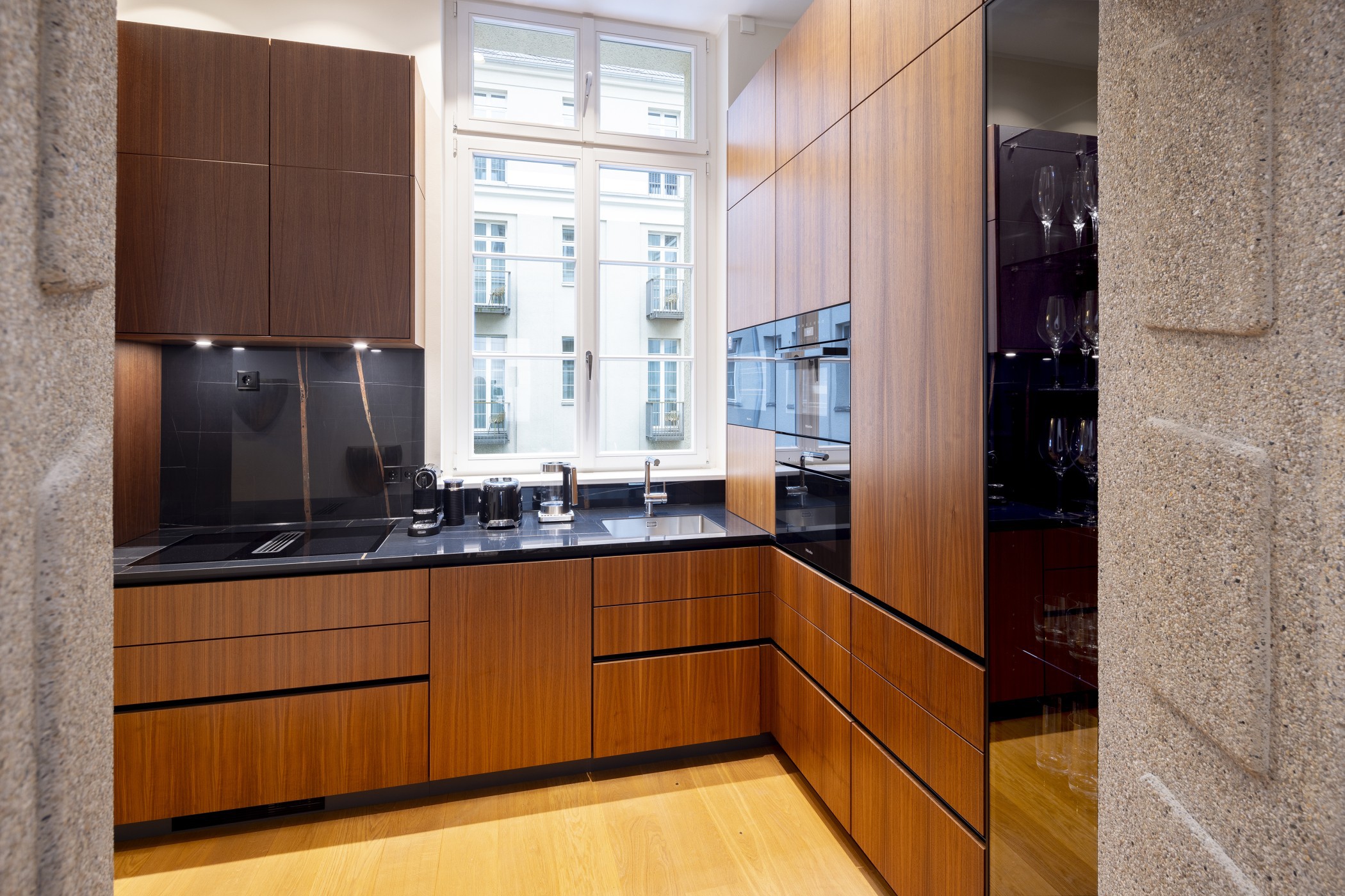 Küche mit Holzfronten, schwarzer Steinarbeitsplatte und Vitrine mit Gläsern