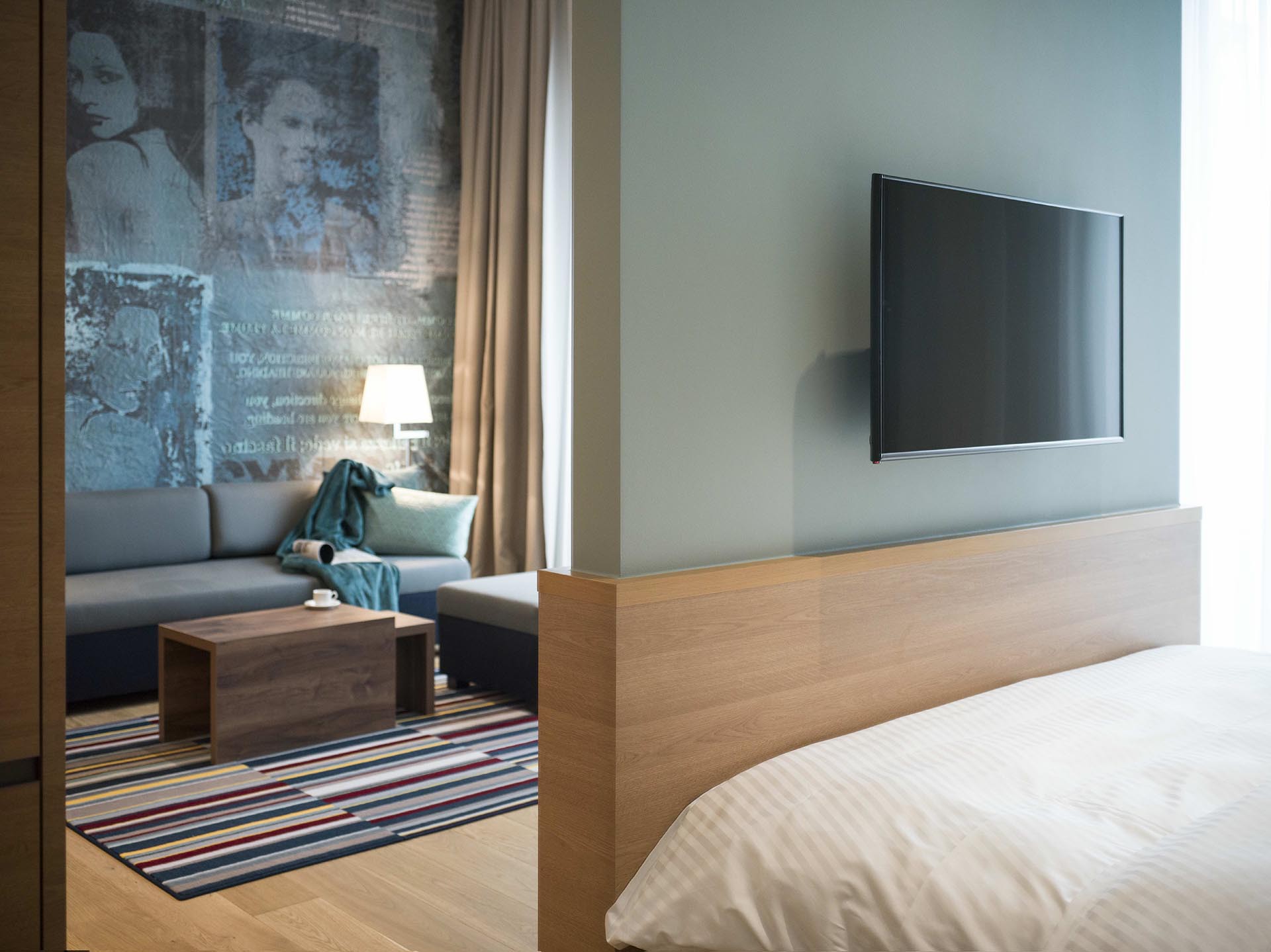 Suite with double bed, TV and seating area in front of a mural with portraits of women