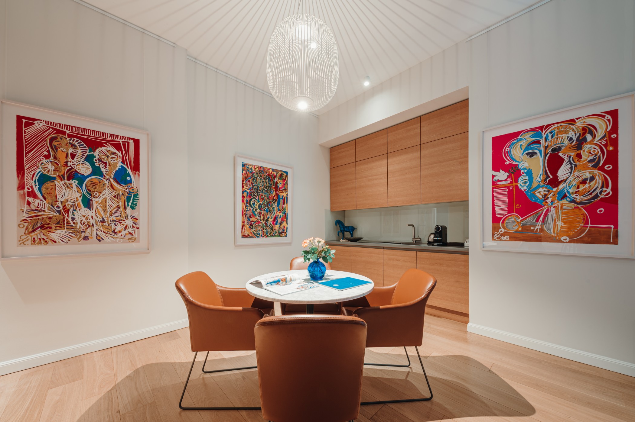 Art Suite dining area with round table, leather chairs and colourful artworks