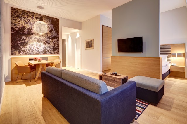 Suite with sofa, dining table, TV and sleeping area behind a half-height wooden partition