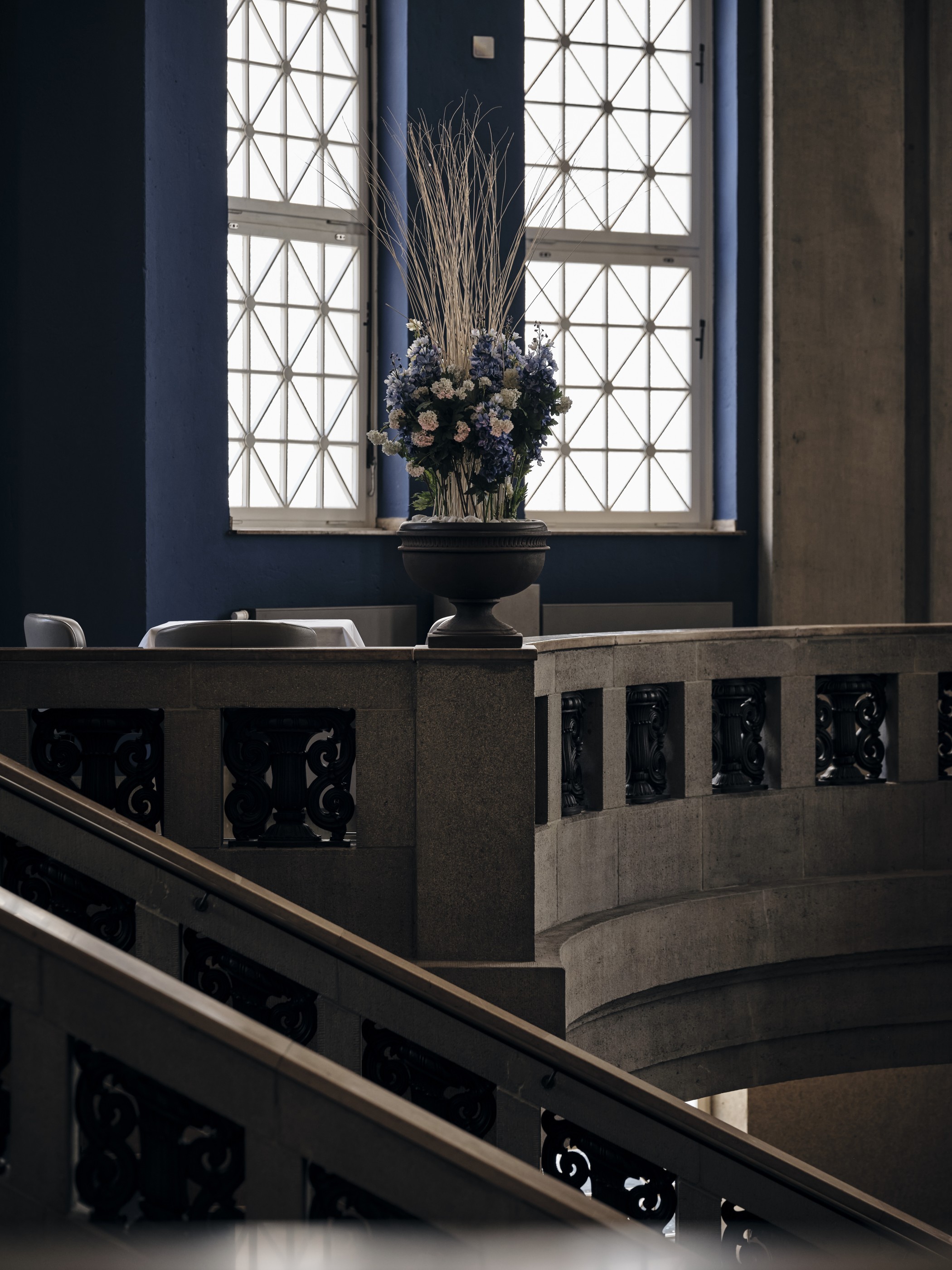Emporenbrüstung mit Ornamentgittern und Treppe vor einem hohen Fenster mit Blumenarrangement