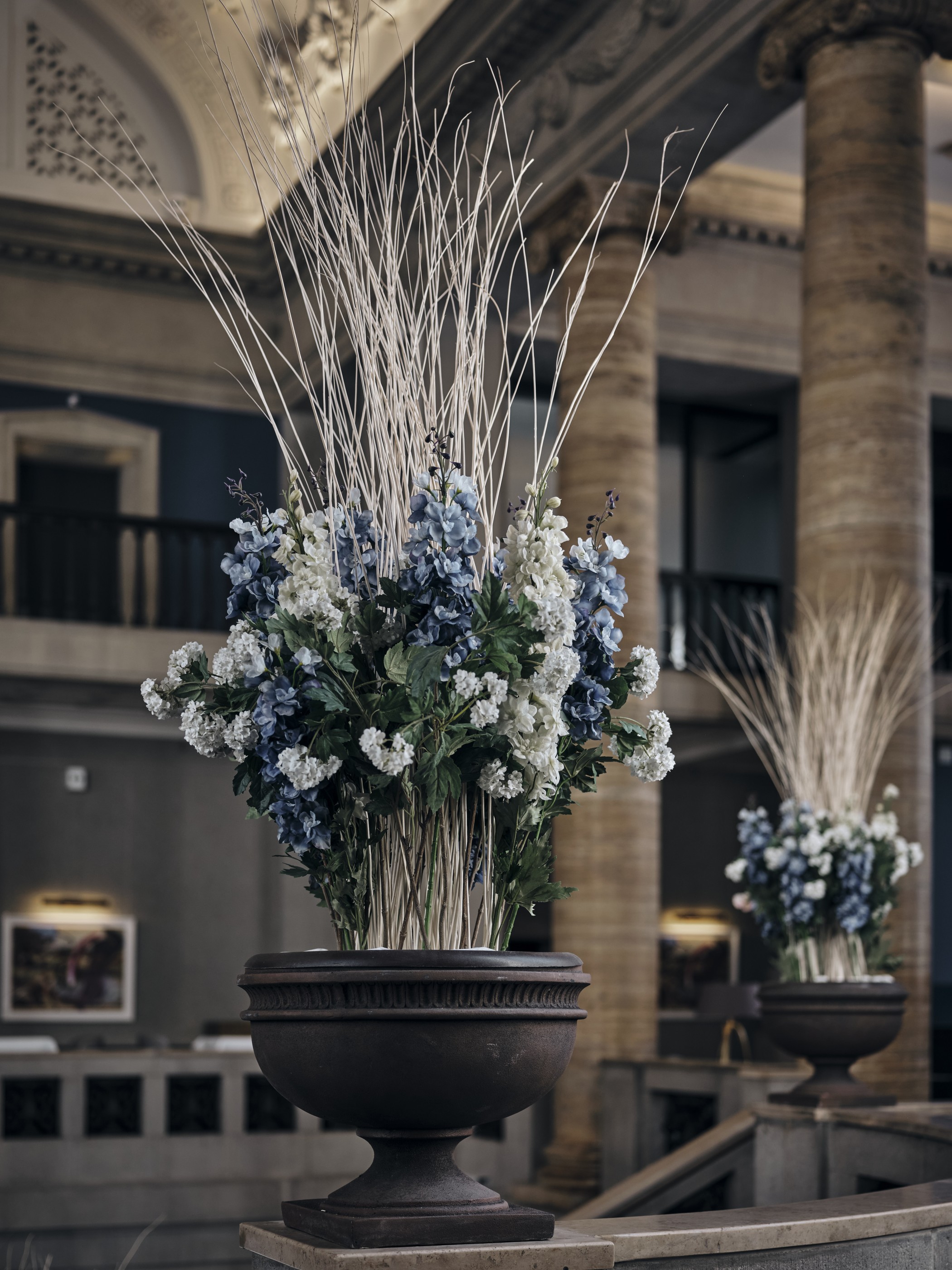 Große Blumenarrangements mit blauen und weißen Blüten in Steinurnen zwischen den Säulen der Empore